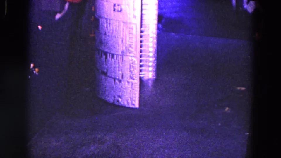 1967 Trenton frame showing the corrugated tube upright on a dark industrial surface, with strong purple-blue film color shift.