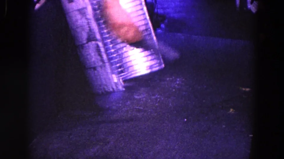 1967 Trenton 8mm frame showing a cropped adult hand and striped sleeve beside a reflective metal object in a dim private interior.