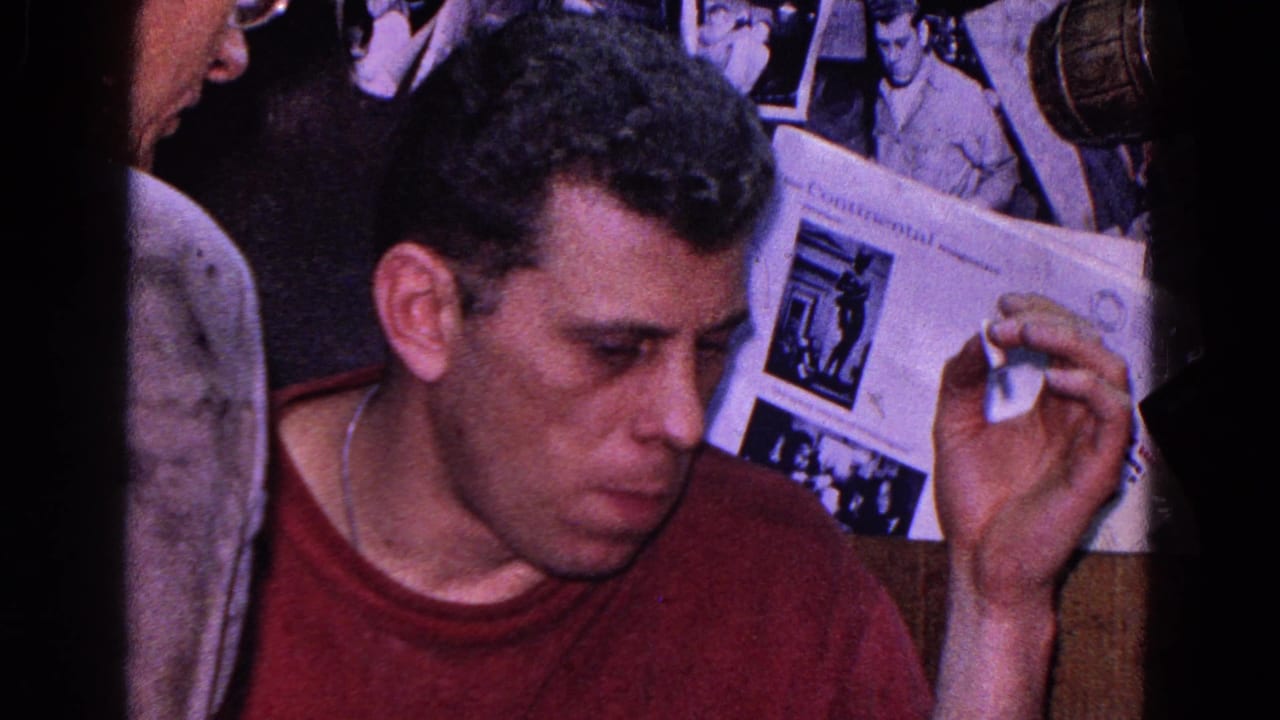 Man in a red shirt holds a cigar or cigarette beside game materials and pinned photographs.