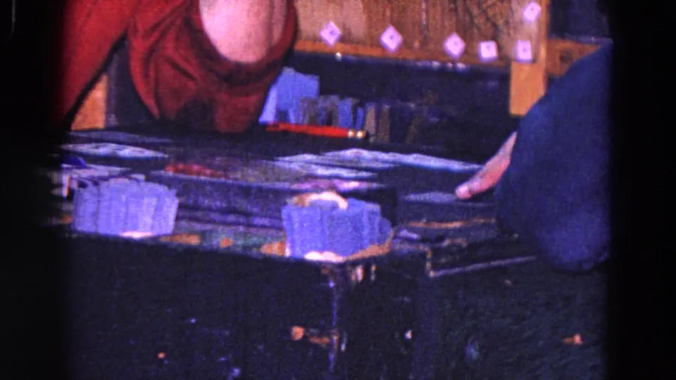 1967 Trenton frame focused on the tabletop game, showing stacked pieces, a player's hand, and a man in a red shirt leaning over the table.