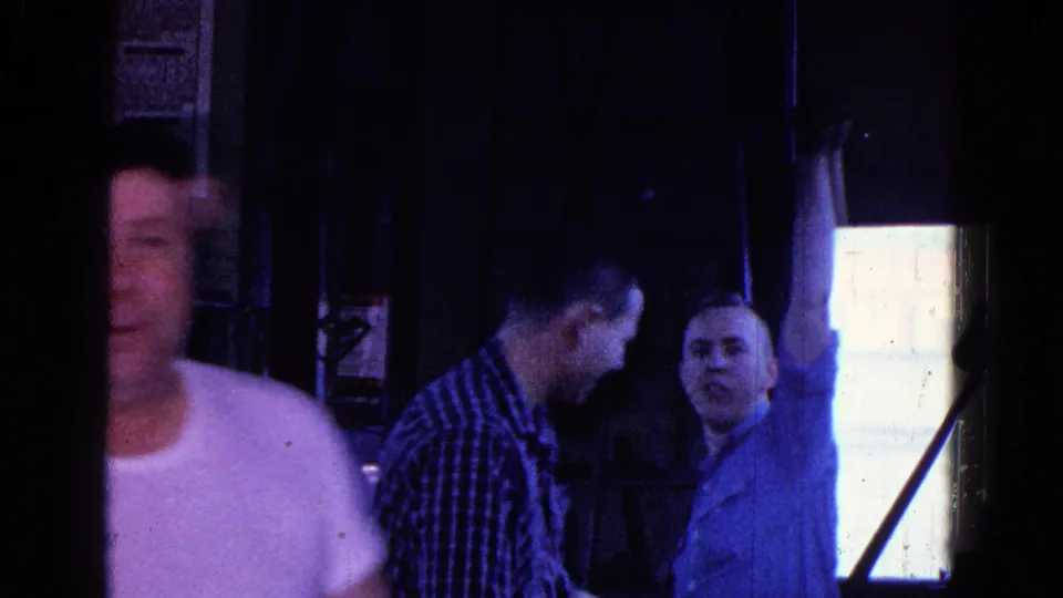 Three adult men appear in the 1967 Trenton workplace interior, one cropped at left and two coworkers near the bright window.