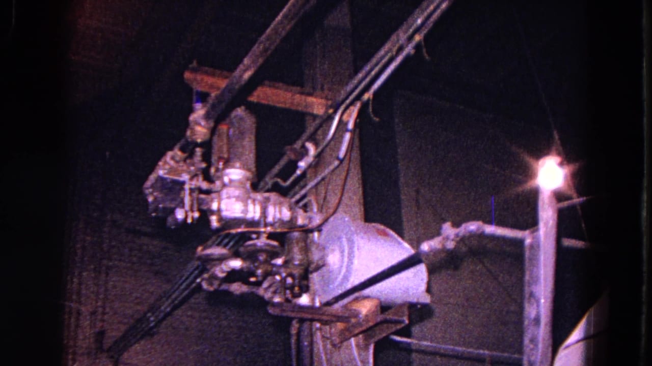 Close view of metal electrical hardware, cables, and a bright light in a dark factory area.