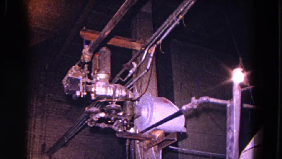 Close 8mm view of factory electrical apparatus in Trenton, with cables, brackets, fittings, and a bright work light in blue-purple exposure.