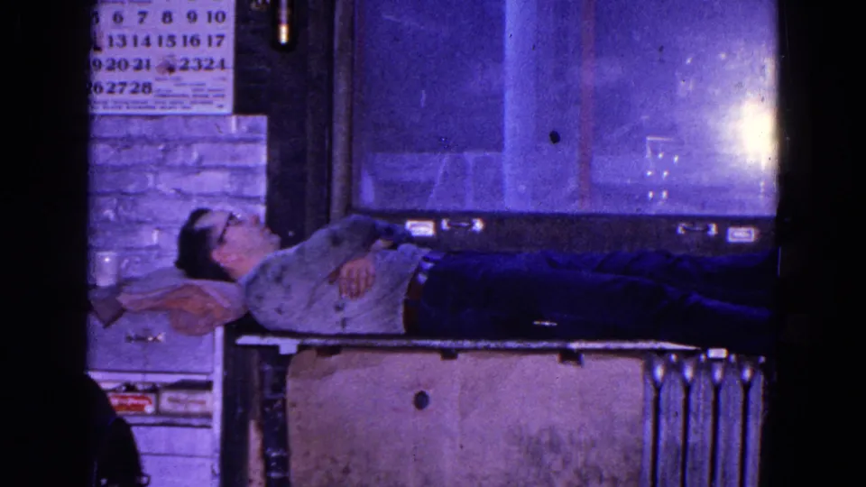 A man in glasses rests on his back on a makeshift bed in the 1967 Trenton factory interior.