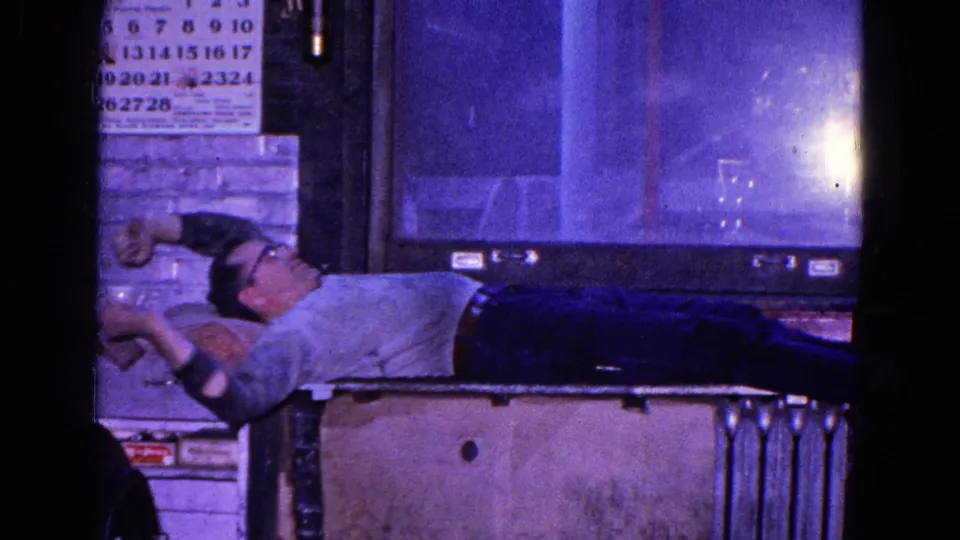 The man stretches while lying on the table in the 1967 Trenton interior, adding a candid gesture of fatigue.