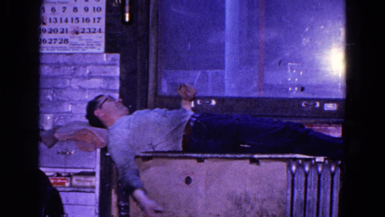 In this 1967 Trenton home-movie frame, a man in glasses reclines near a window and calendar in a dim interior.