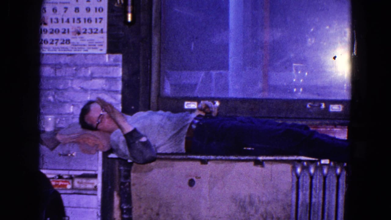 Man reclines near the window and raises one arm while resting on a box or bench.