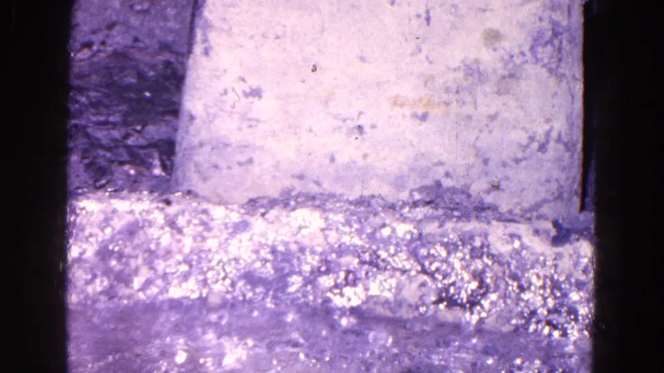 The frame drops lower in the dim interior, showing the box front, wall surface, floor, and only a partial glimpse of the figure.