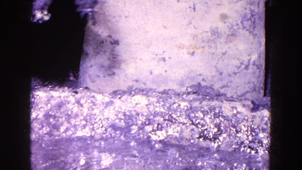 1967 Trenton 8mm frame showing bright ripples on a silvery liquid surface beside a pale textured block.
