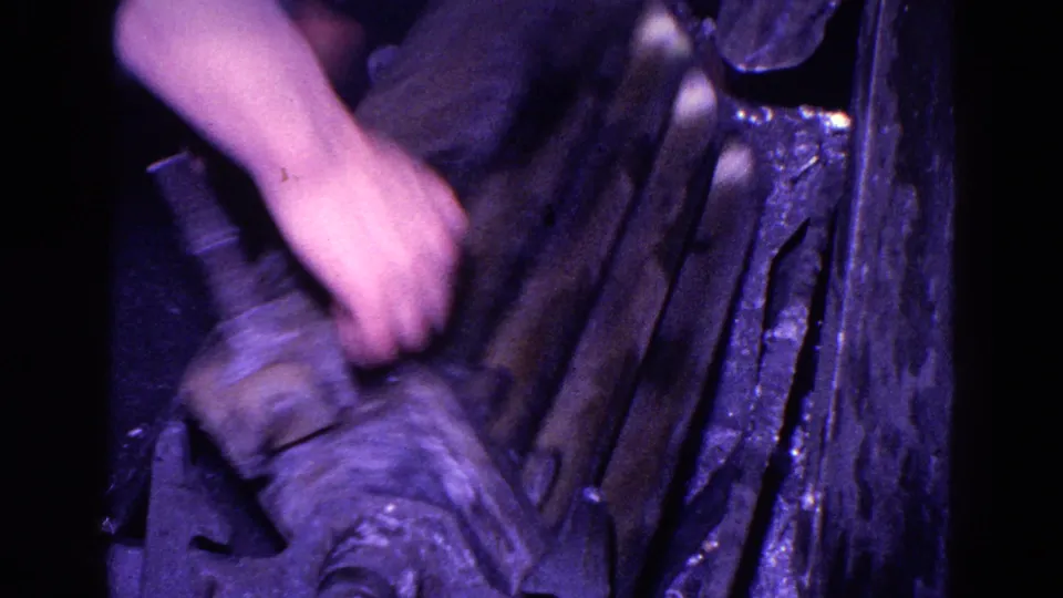 Worker's hand operates or adjusts dark metalworking machinery during a 1967 Trenton casting process filmed on 8mm.