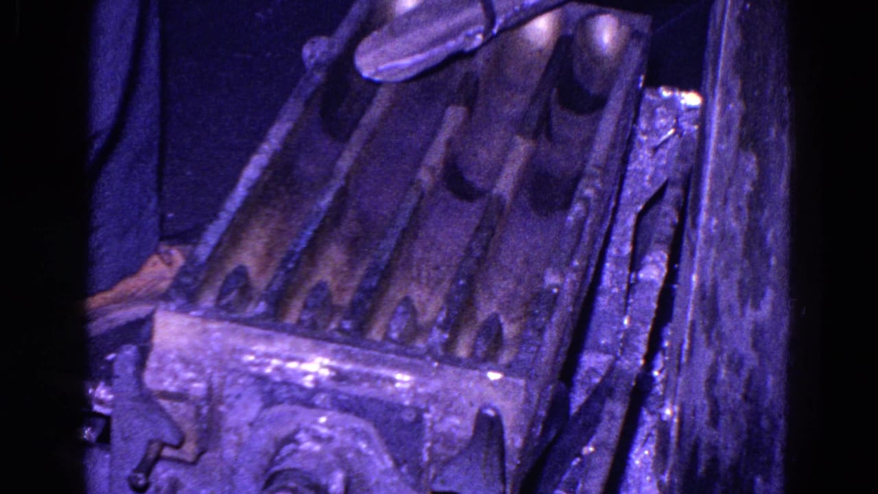 Close view of angled metal chutes with dark worn surfaces and purple-tinted lighting.