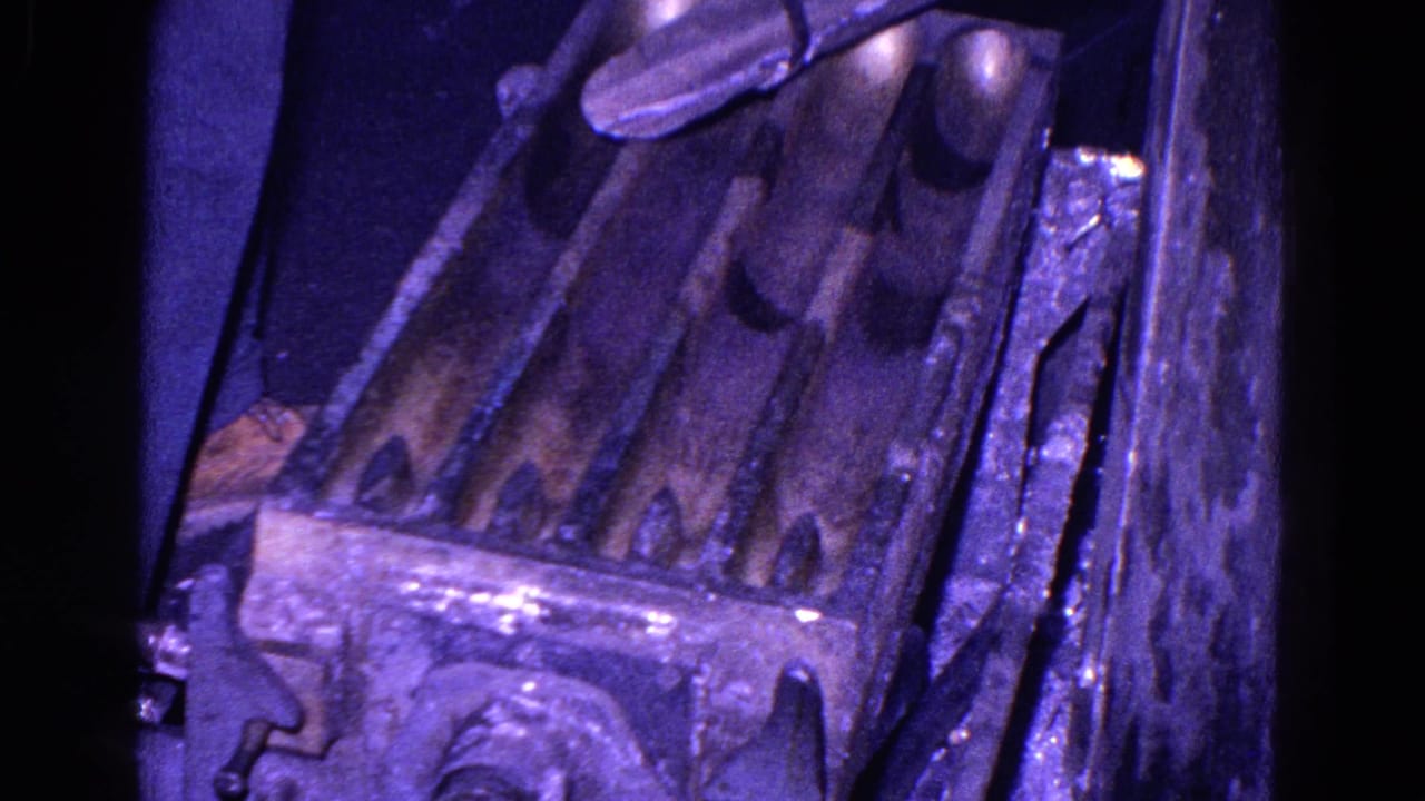 1967 Trenton 8mm frame of industrial metal troughs and adjacent panels, with dense grain and a purple color cast.