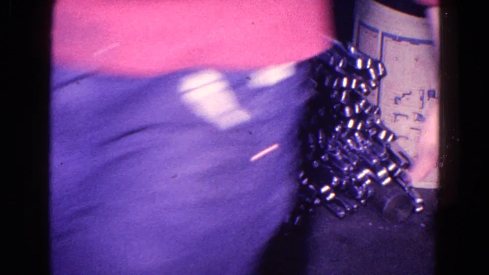 A blurred worker or visitor torso crosses the 1967 Trenton factory frame beside stacked metal components and a marked container.