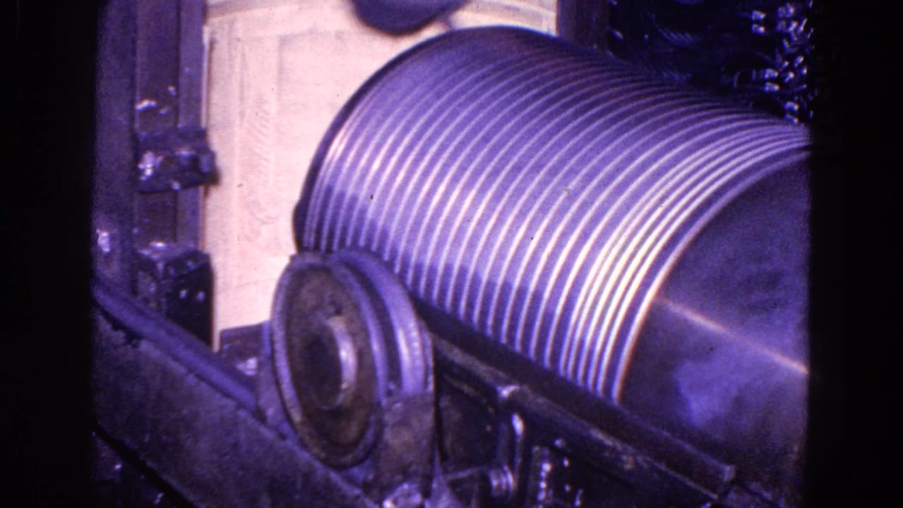 Ribbed machine roller with partial worker clothing at the top of frame.