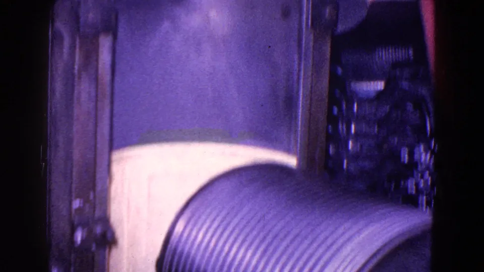 Purple-cast 8mm frame showing the ribbed roller at the lower edge and shadowed mechanical components behind the machine housing.
