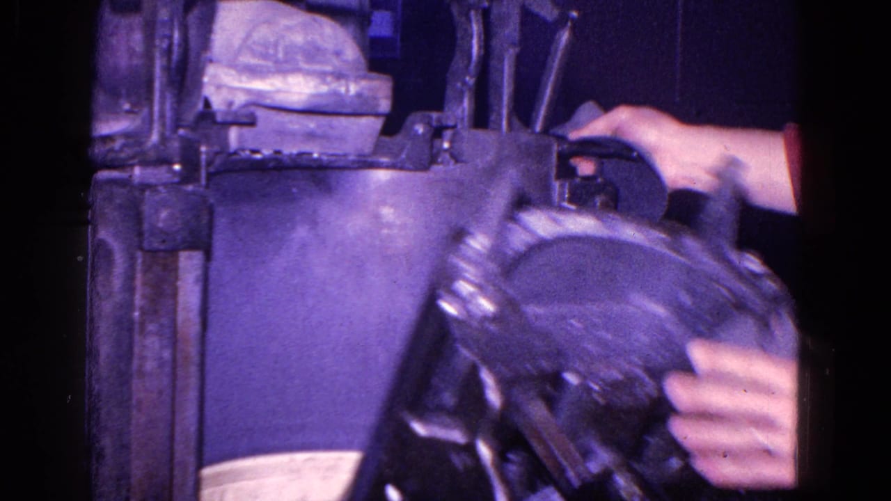Worker's hands operate a large metal machine in dim light.