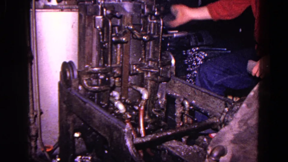 A red-shirted worker is partly visible beside a large industrial machine in the 1967 Trenton 8mm footage.