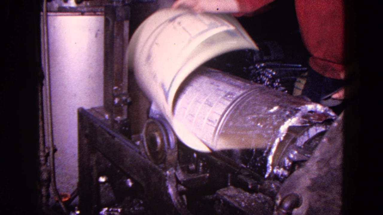 The canister rotates on an industrial machine, with peeled outer material visible at one end and the worker standing nearby.