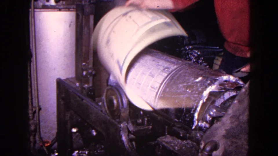 The canister rotates on an industrial machine, with peeled outer material visible at one end and the worker standing nearby.
