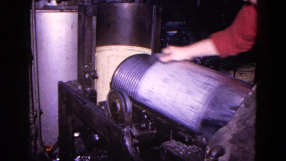 The worker's sleeve blurs with motion as the canister rotates on the machine, showing a close view of manual factory operation.