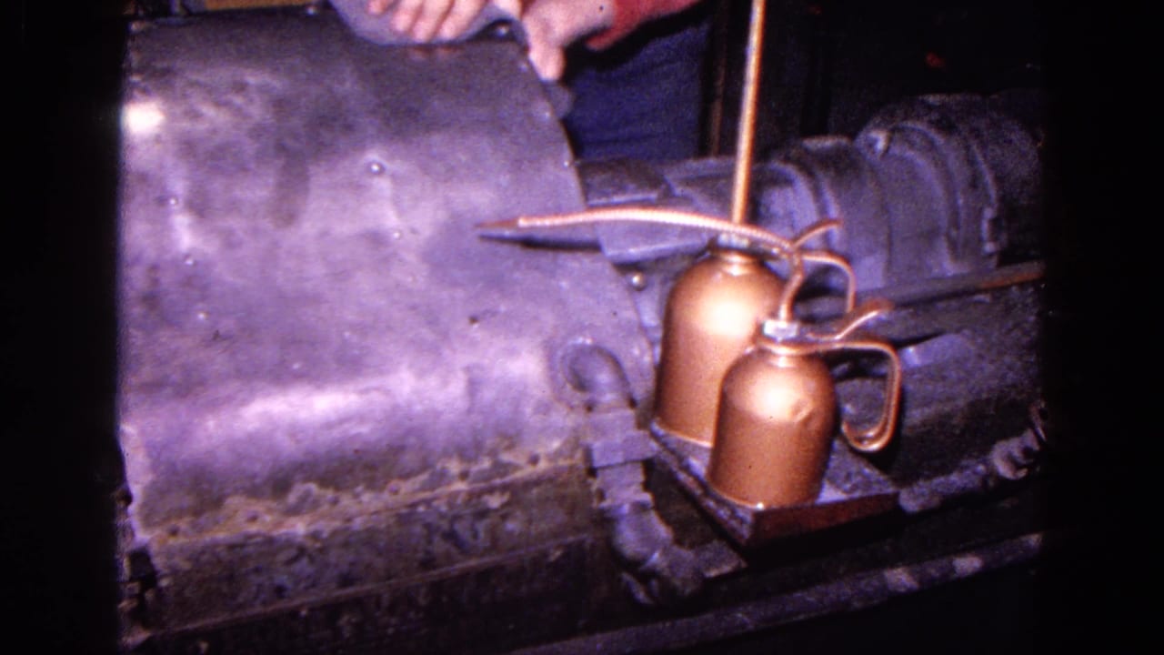 Metal shaping machine with copper oil cans and a worker's hands partly visible above it.