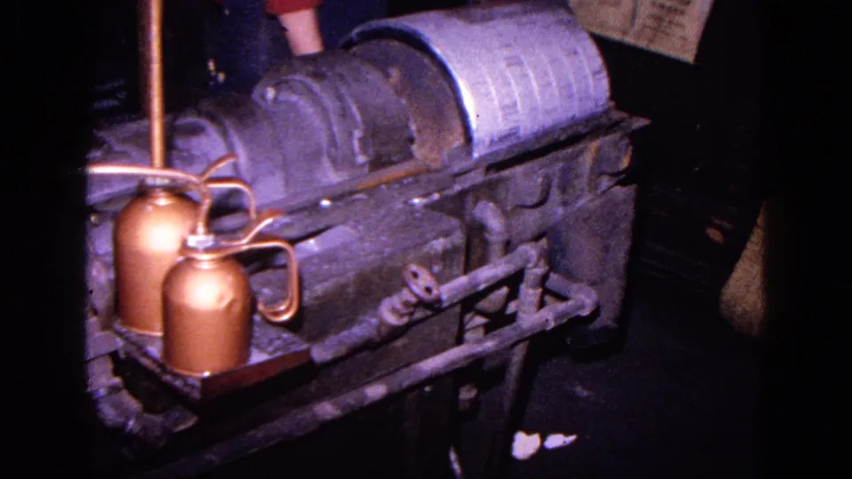 Side angle on a 1967 industrial metal shaping machine, with a cylindrical component, copper oil cans, and pipes visible.