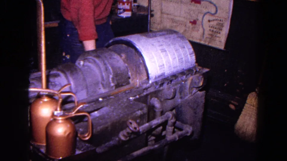 1967 Trenton factory frame with a worker in a red sweater beside metal shaping equipment and a schematic diagram on the wall.