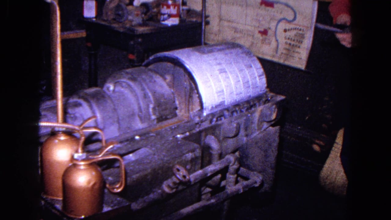 Large gray machine and white linen roll with a worker partly visible at the right edge.