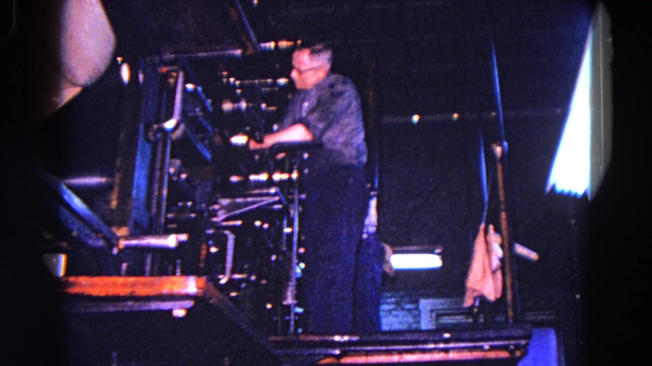 Worker leans toward the industrial press controls in a dark machine area.