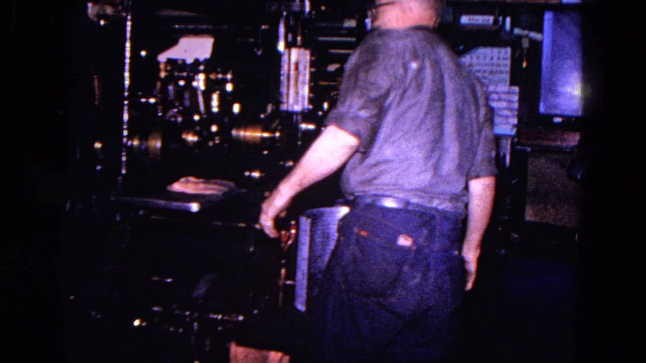 1967 Trenton factory footage shows an adult worker from behind near large, dimly lit industrial equipment.