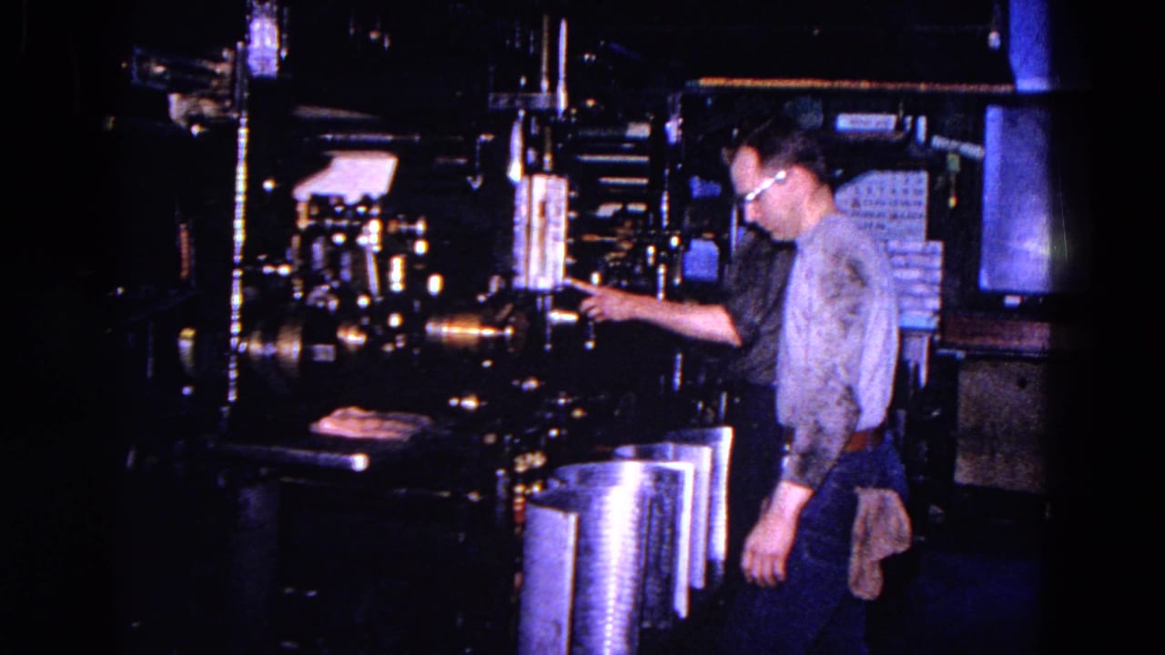 Adult man with glasses reaches toward a large machine.