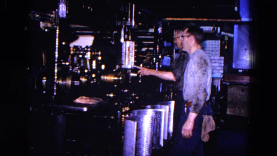 A 1967 home-movie frame shows a worker beside heavy factory machinery and bright metal components in Trenton.