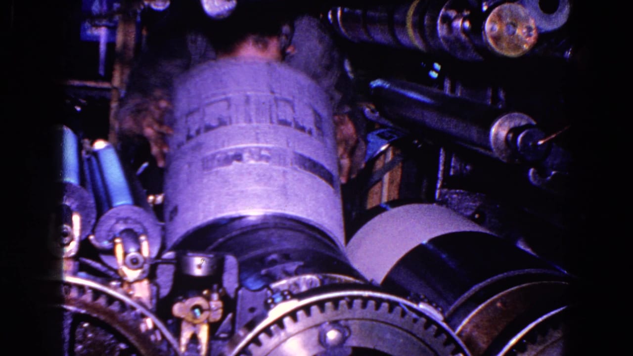 From a close handheld angle, a worker is seen from behind near a large cylinder and surrounding factory machinery.