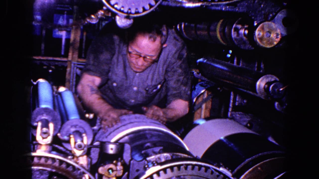 In 1967 Trenton, New Jersey footage, a man in glasses works over exposed gears and rollers on a large industrial machine.