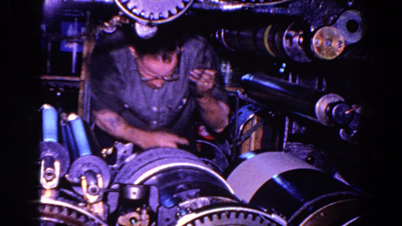 Mechanic looks down and raises one hand while working inside a machine.