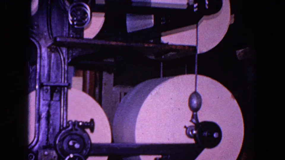 Industrial paper rolls appear behind black metal arms and rollers in this 1967 Trenton 8mm footage frame.