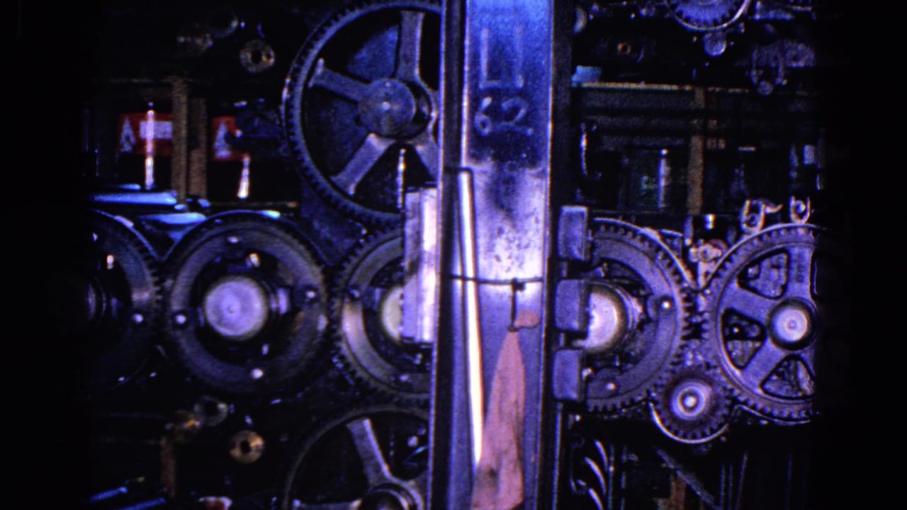 Close view of dark printing-press machinery with gears, rollers, and a vertical metal support.