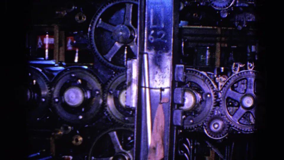 1967 8mm close-up from Trenton showing exposed gears, rollers, and metal supports on an operating industrial press.