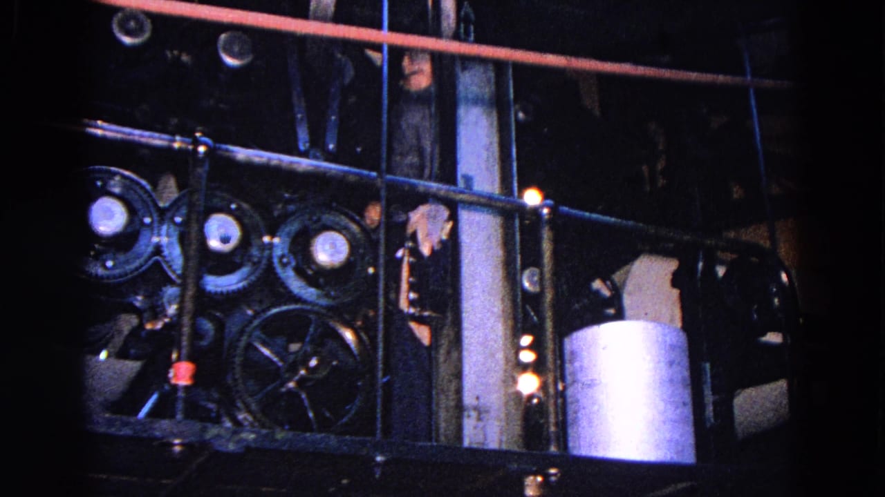 Close 1967 Trenton view of press machinery with rods, gears, a paper roll, and a partially visible worker behind the equipment.