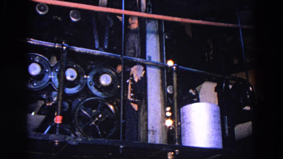 Close 1967 Trenton view of press machinery with rods, gears, a paper roll, and a partially visible worker behind the equipment.