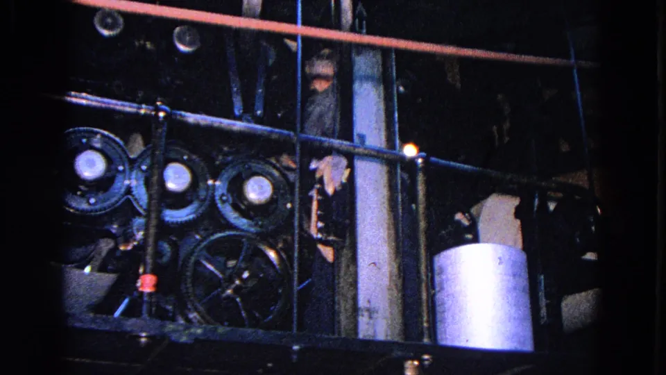 1967 Trenton factory interior with a worker partly visible behind railings near exposed machinery and a metal cylinder.