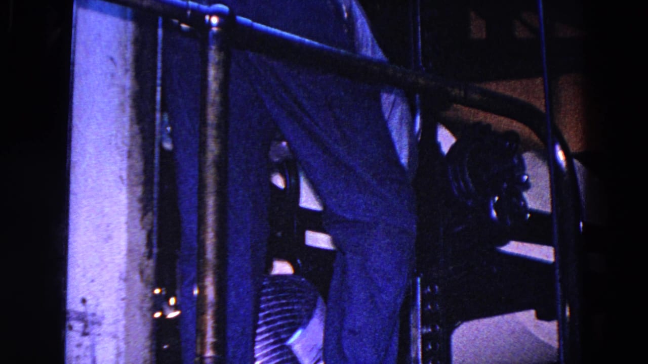 Blue-tinted 1967 Trenton factory footage showing dark newspaper or paper machinery, metal bars, and paper surfaces in a dim interior.