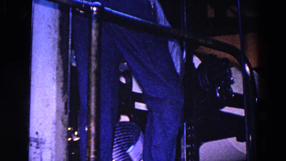 Blue-tinted 1967 Trenton factory footage showing dark newspaper or paper machinery, metal bars, and paper surfaces in a dim interior.