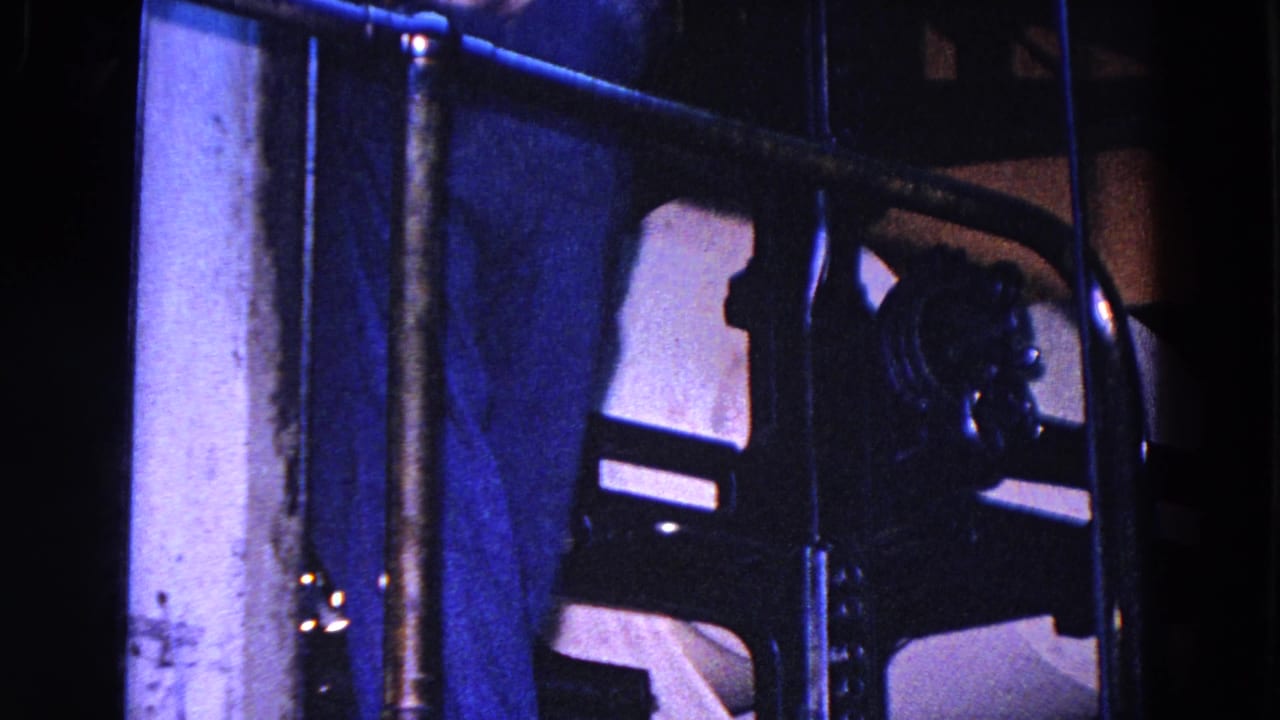 Close view of dark industrial machinery, bars, and paper in low blue light.
