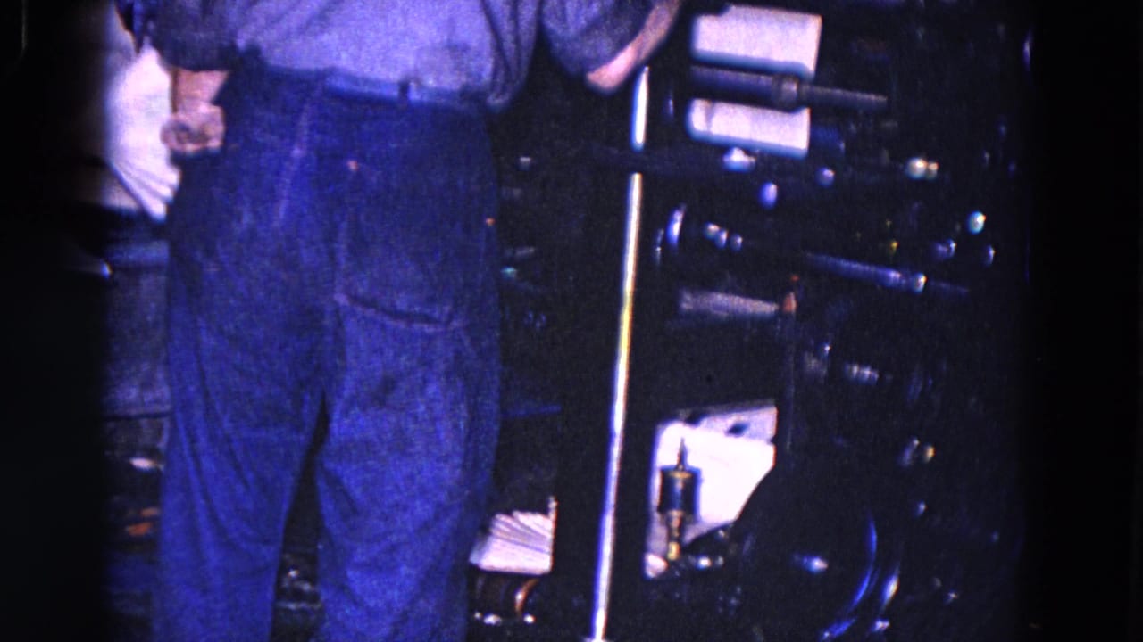 Adult worker in blue work pants stands beside newspaper or paper machinery in the 1967 Trenton factory footage.