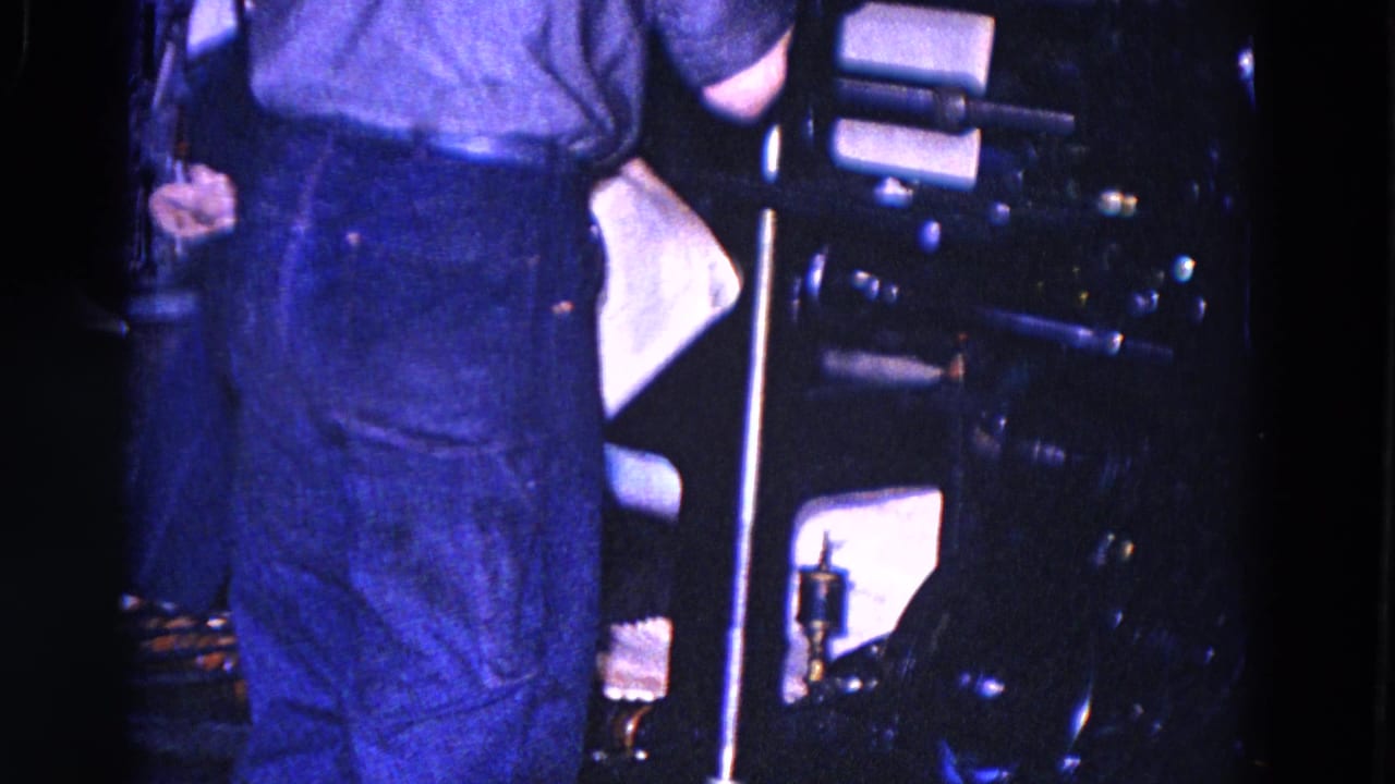 Worker stands beside a dark printing press with paper and metal supports visible.