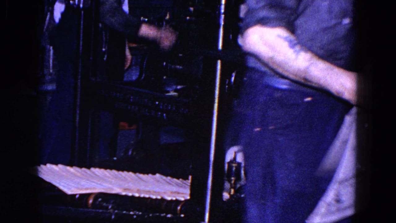 A worker stands near stacked newspapers and dark press machinery inside the Trenton printing facility.