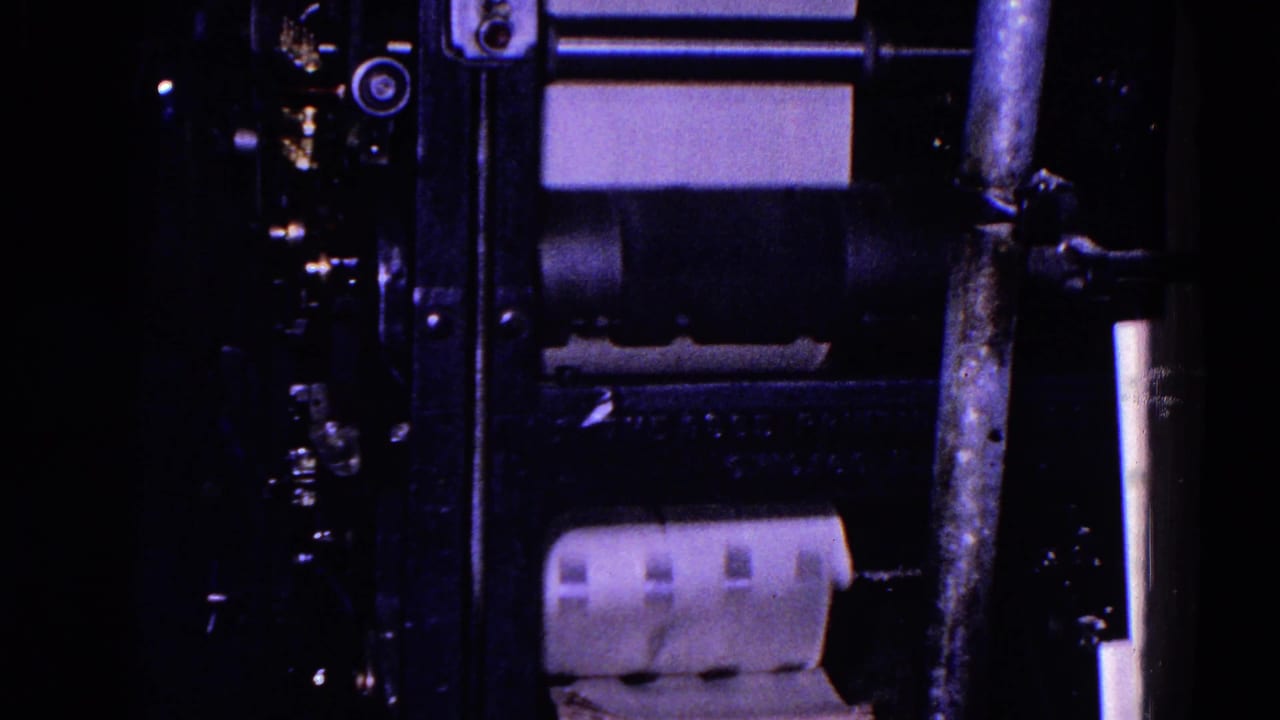 Paper feeds through dark rollers on a printing press.