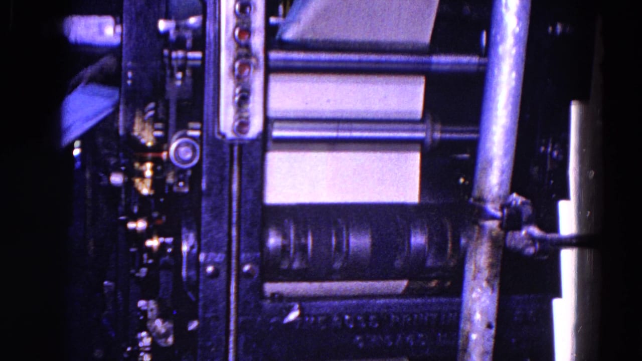 The printing press rollers and paper path fill the frame, with a partially visible worker or operator at the left edge near the machinery in the 1967 Trenton factory footage.