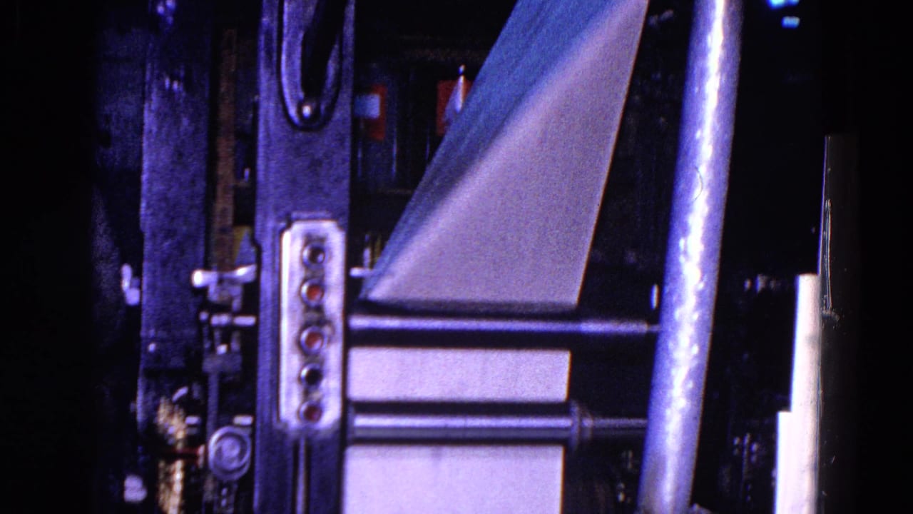 Close view of printing press machinery with metal supports, rollers, and angled paper feed sheets.